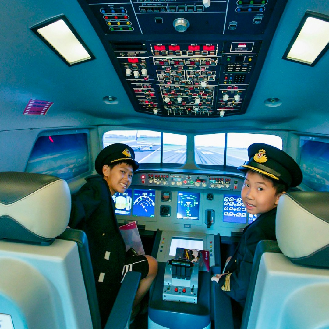 Children in pilot uniforms inside a flight simulator at Kidzania Bangkok.