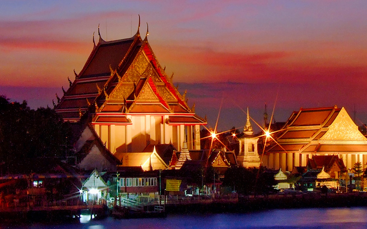 Chao Phraya River at sunset with illuminated temple, Bangkok, Thailand.