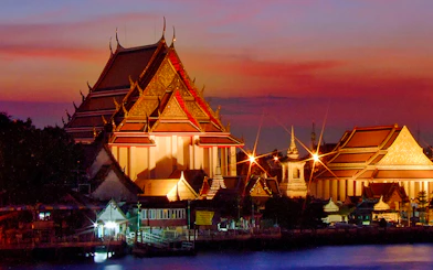 Chao Phraya River at sunset with illuminated temple, Bangkok, Thailand.