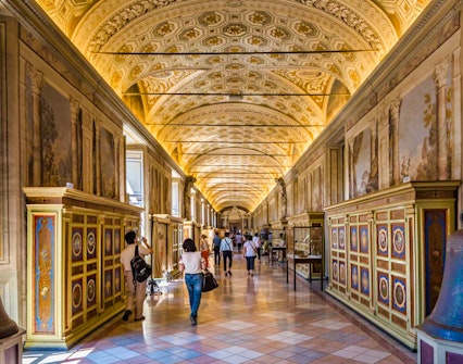 Visitors walking through ornate corridor in Vatican Museums, Vatican City.