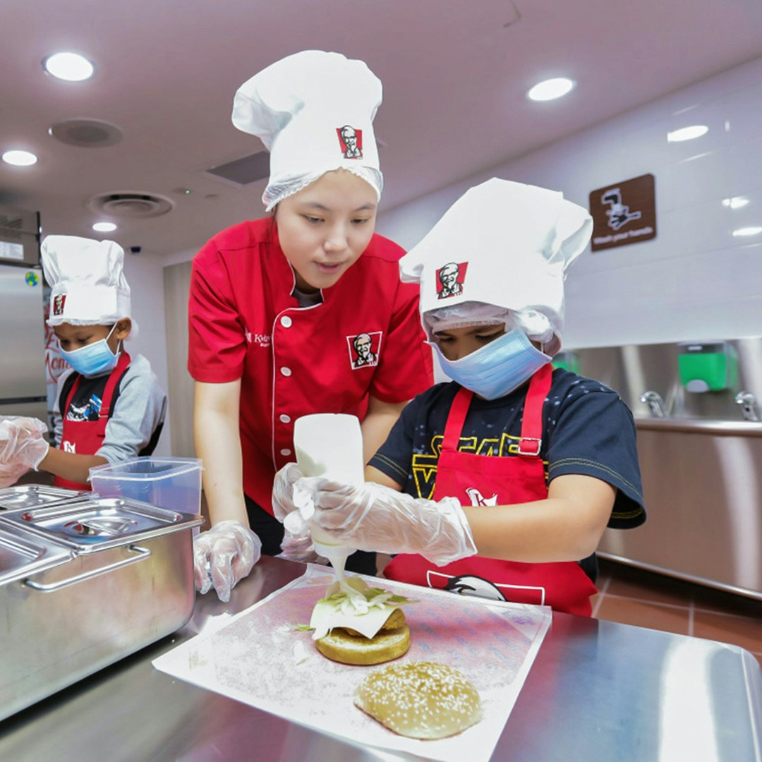 Children making burgers at KidZania with guidance from an instructor.