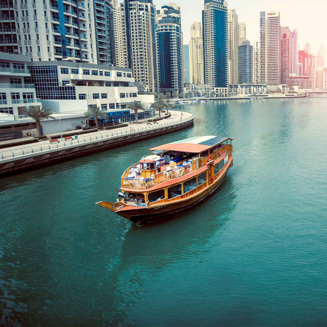 Dhow boat cruising along Dubai Creek with city skyline in the background.