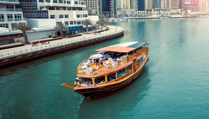 Dhow boat cruising along Dubai Creek with city skyline in the background.