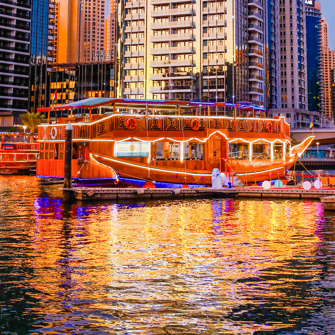 Dhow boat illuminated at night in Dubai Marina, reflecting on the water.