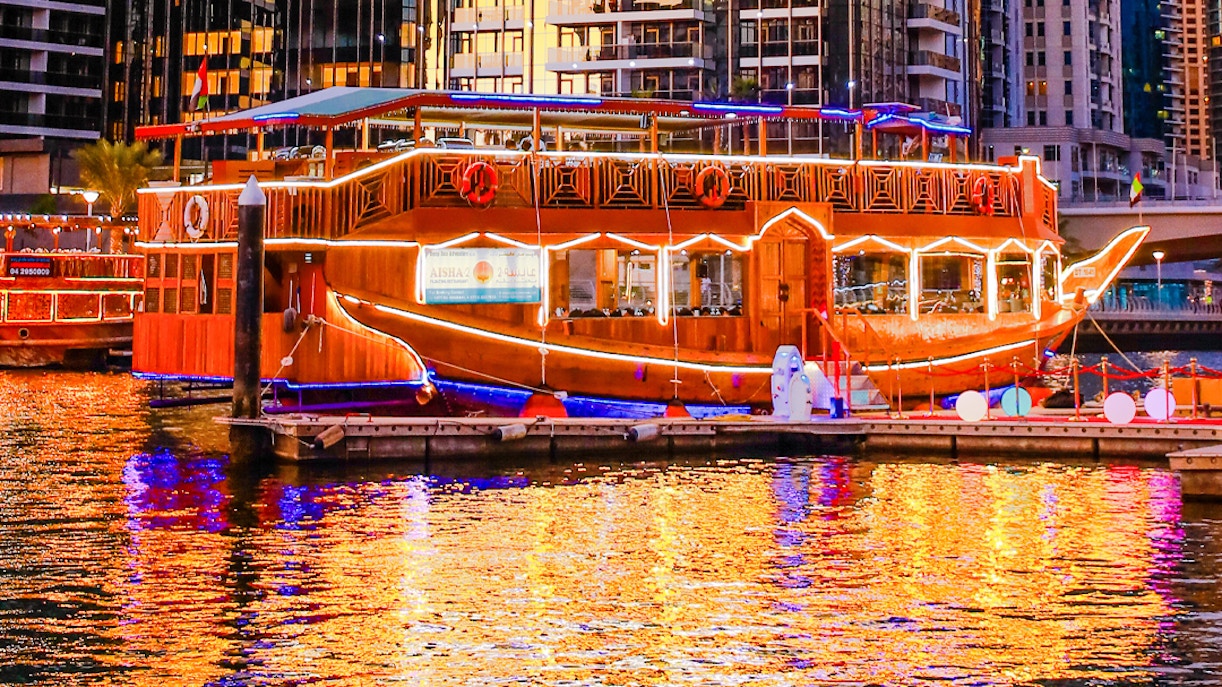 Dhow boat illuminated at night in Dubai Marina, reflecting on the water.
