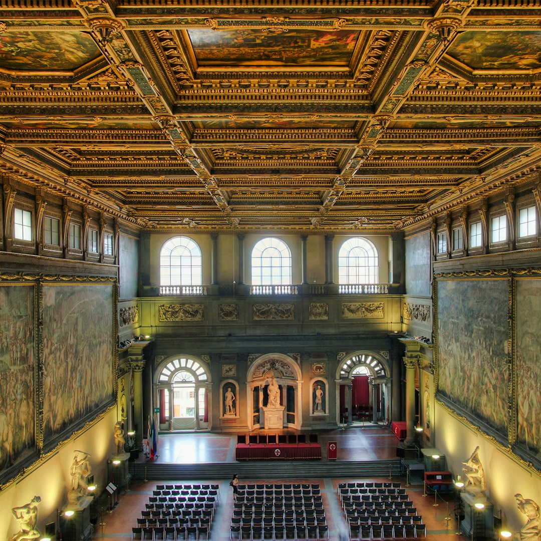 Interior of Florence's Palazzo Vecchio with ornate ceiling and large frescoes.