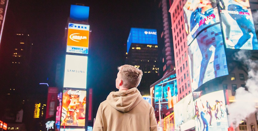 Person standing in Times Square, New York City, surrounded by bright billboards at night.