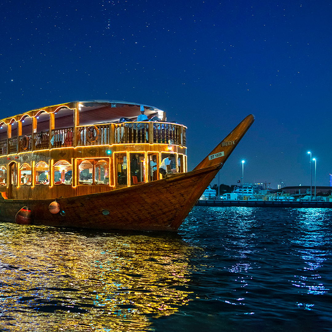 Dhow cruise on Dubai Creek at night with city lights reflecting on water.