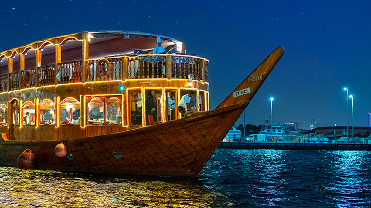 Dhow cruise on Dubai Creek at night with city lights reflecting on water.