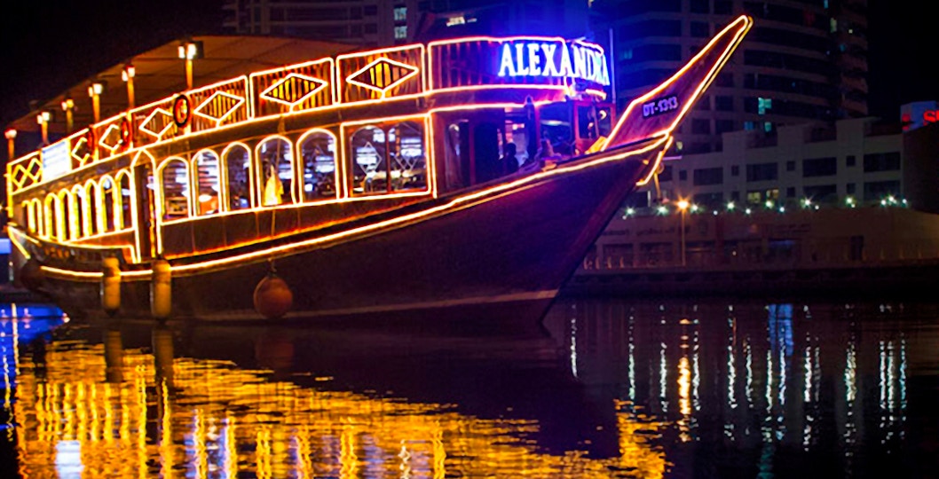 Dhow cruise with lights reflecting on Dubai Marina at night.