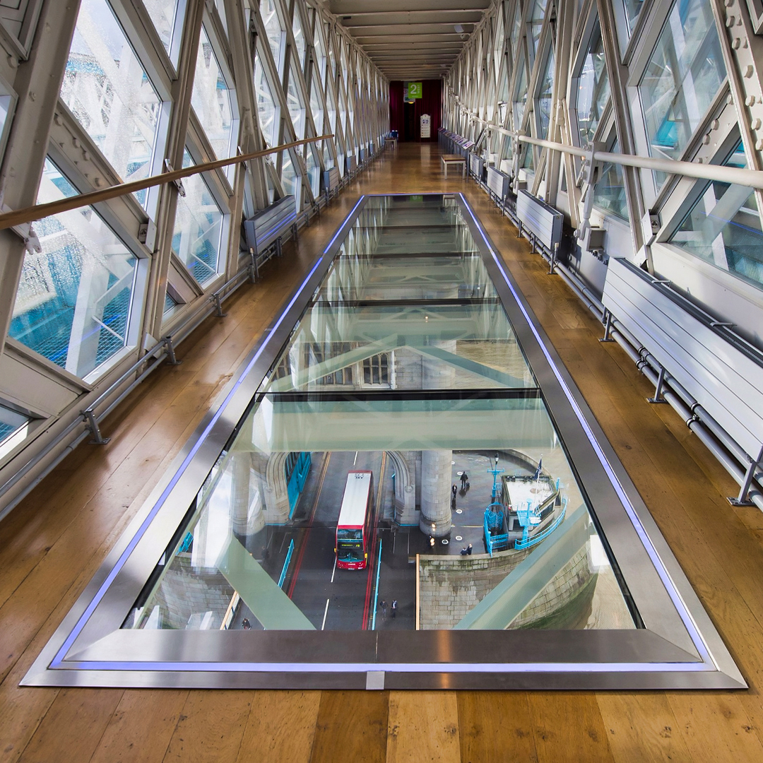 Glass walkway inside Tower Bridge, London, overlooking road and red bus below.