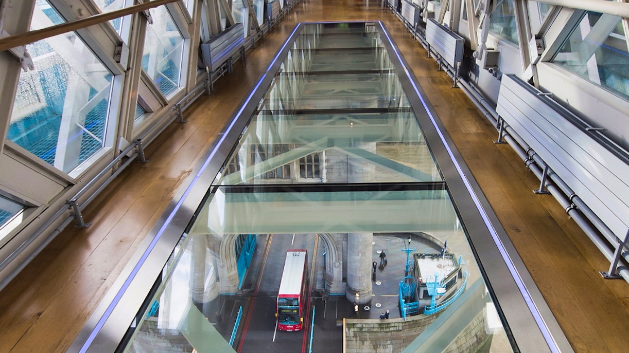 Glass walkway inside Tower Bridge, London, overlooking road and red bus below.