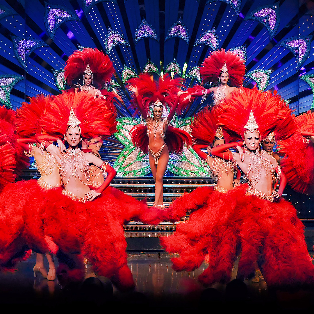 Dancers performing at Moulin Rouge in Paris with vibrant costumes and feathered headdresses.