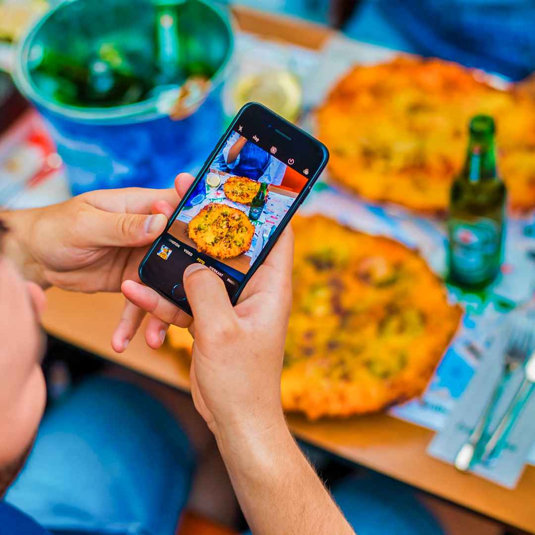 Person photographing pizza and drinks on Amsterdam cruise table.