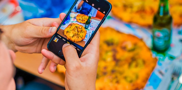 Person photographing pizza and drinks on Amsterdam cruise table.