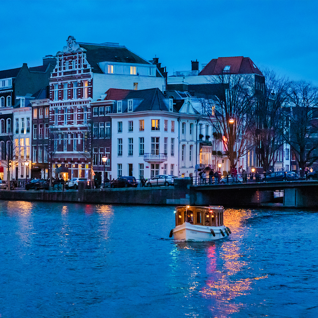Evening canal cruise boat on Amsterdam canal with illuminated buildings.