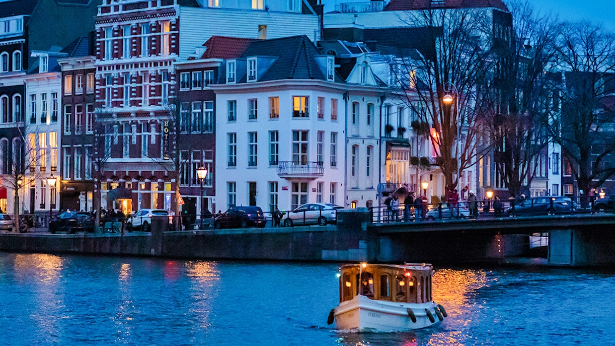 Evening canal cruise boat on Amsterdam canal with illuminated buildings.