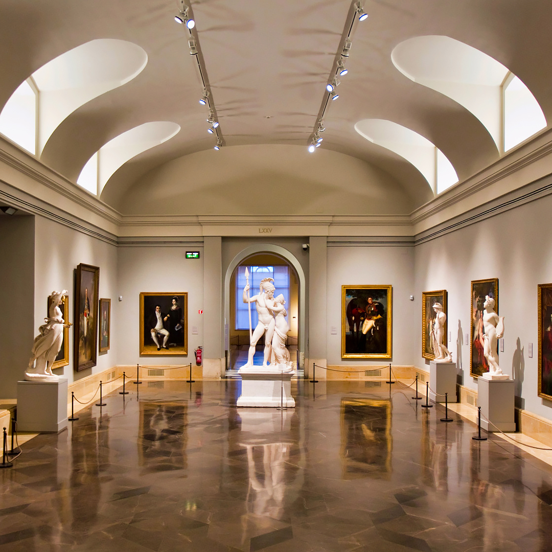 Prado Museum gallery with classical sculptures and paintings on display.