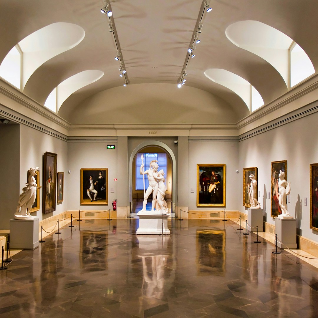 Prado Museum gallery with classical sculptures and paintings on display.