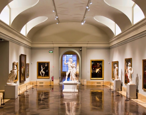 Prado Museum gallery with classical sculptures and paintings on display.
