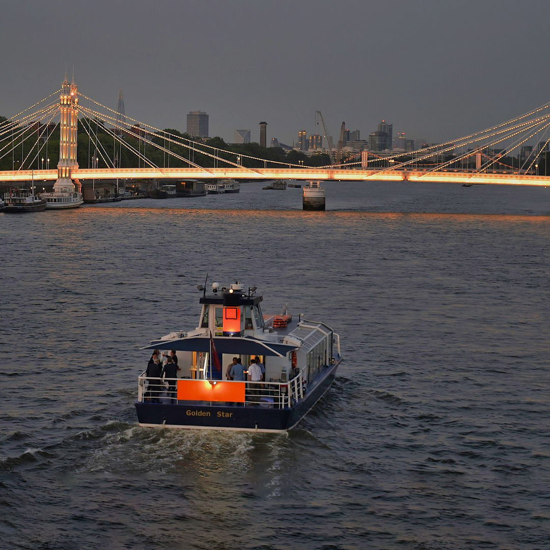 Uber Boat by Thames Clippers cruising near illuminated London bridge at dusk.