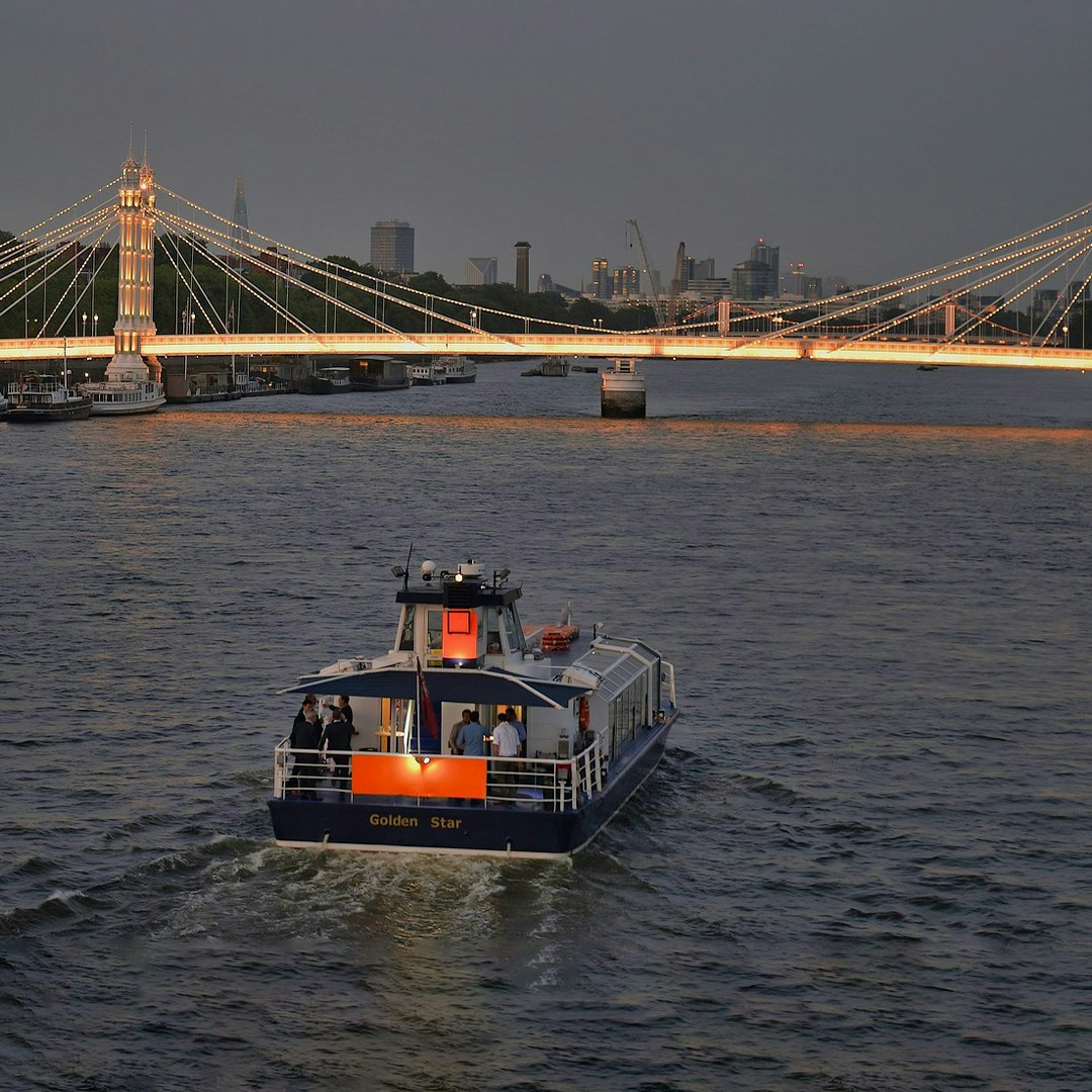 Uber Boat by Thames Clippers cruising near illuminated London bridge at dusk.