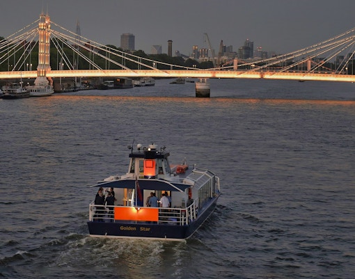 Uber Boat by Thames Clippers cruising near illuminated London bridge at dusk.