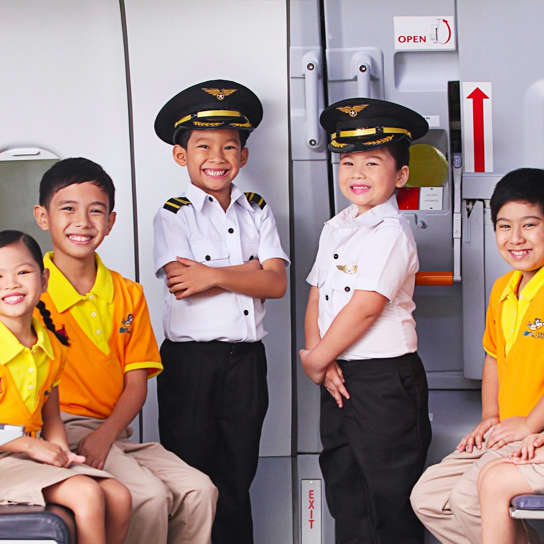 Children in pilot uniforms and yellow shirts at KidZania Singapore airplane exhibit.
