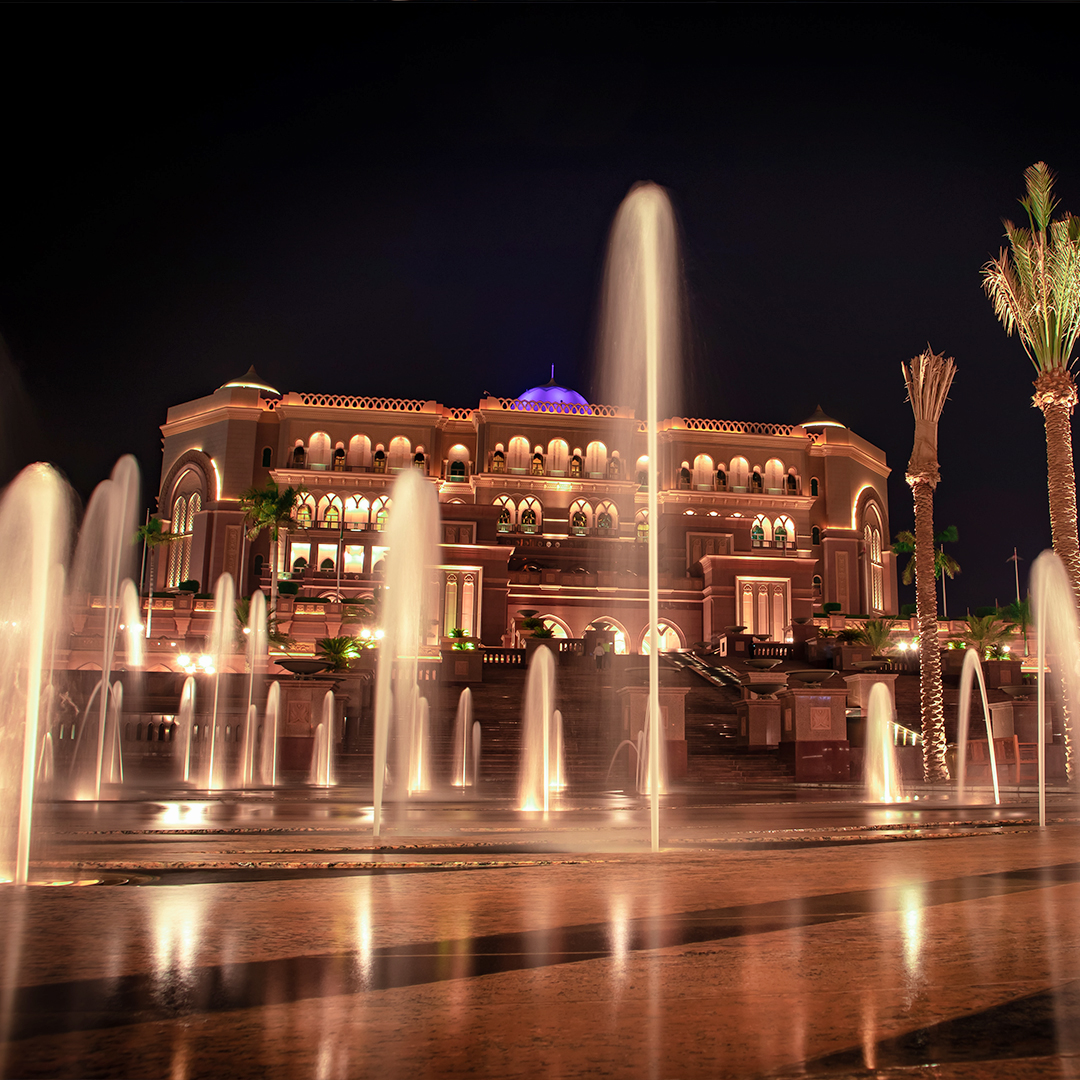 Dubai Fountain Boardwalk at night with illuminated fountains and a grand building in the background.