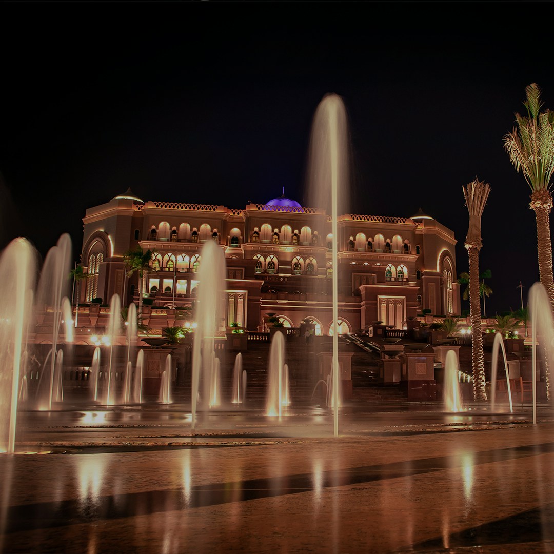 Dubai Fountain Boardwalk at night with illuminated fountains and a grand building in the background.