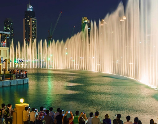 Crowd watching Dubai Fountain show near Burj Khalifa at night.
