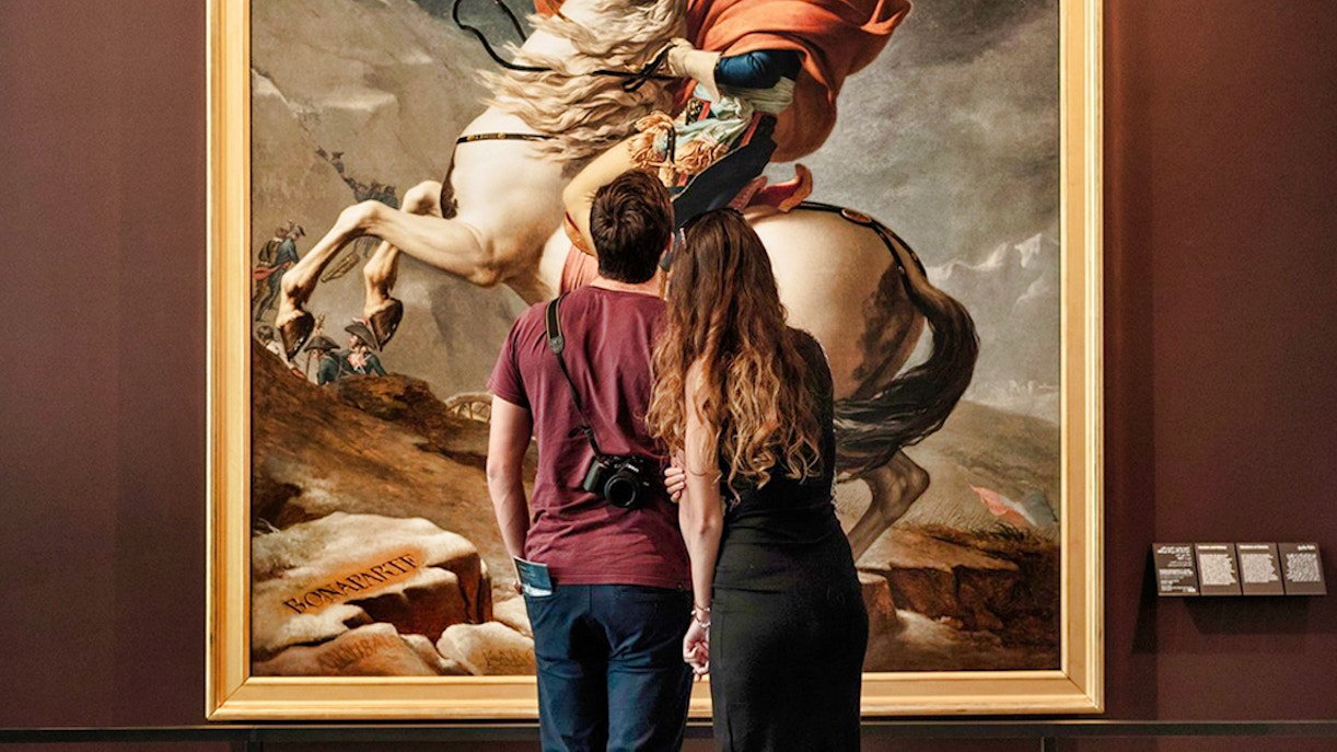 Visitors admiring Napoleon painting at Louvre Abu Dhabi during guided tour.