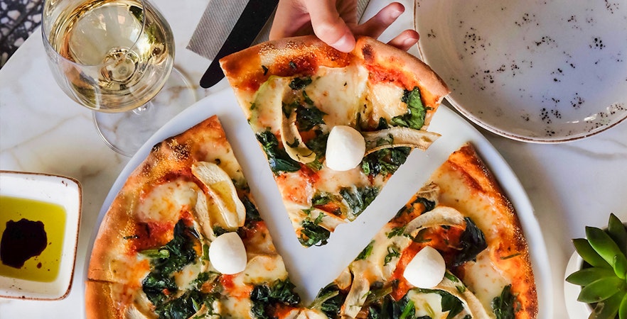 Pizza with mozzarella and greens on a table during a pizza-making course.