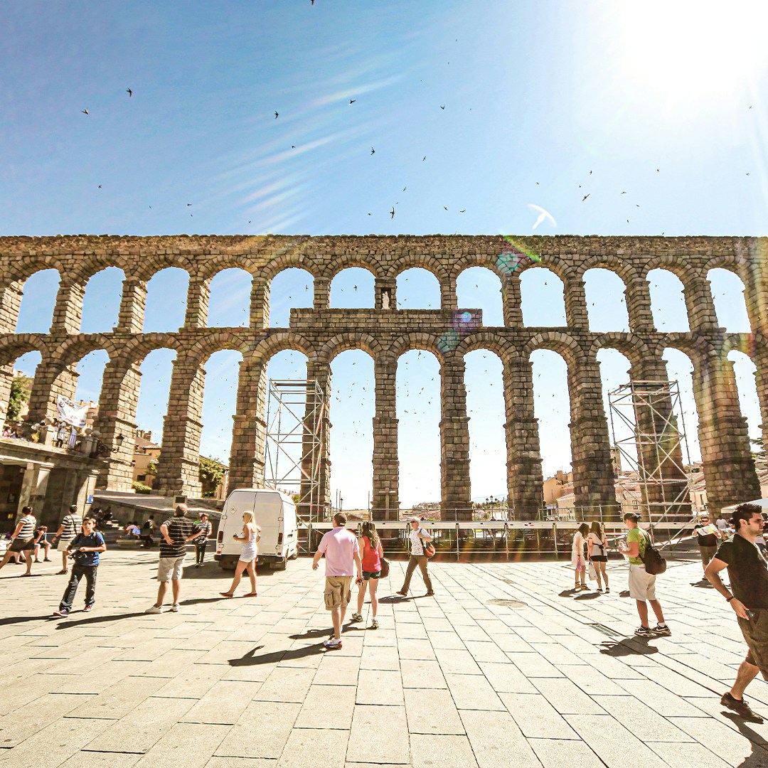 Ancient aqueduct in Toledo with tourists walking beneath a clear blue sky.