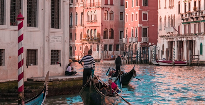 Gondolas navigating a canal in Venice with historic buildings in the background.