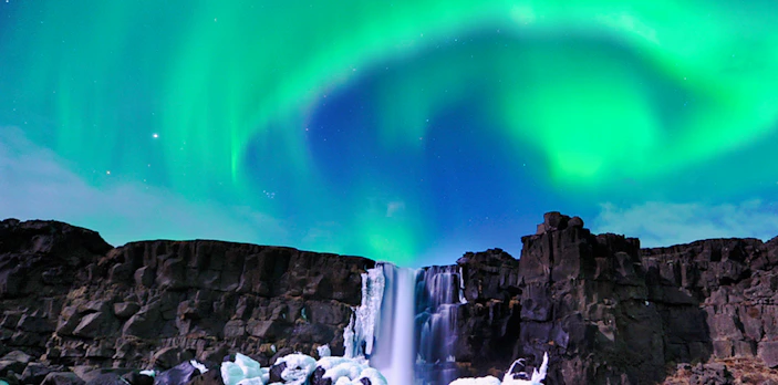 Northern Lights over waterfall near Reykjavik on Aurora Borealis bus tour.